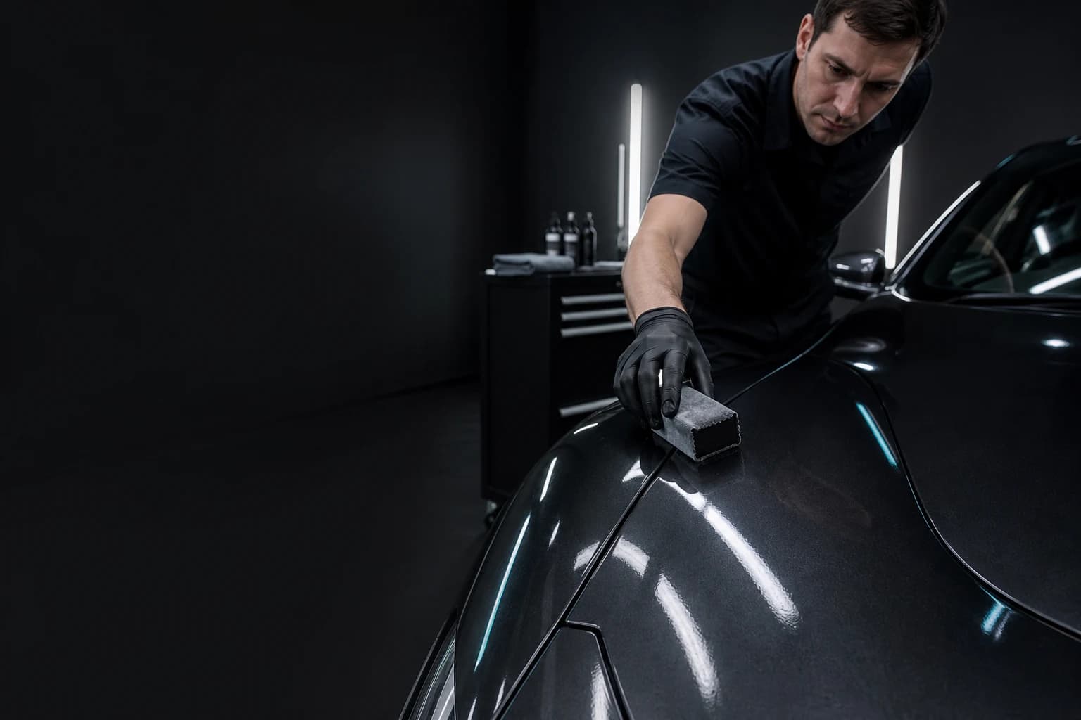 Ceramic coating specialist applying coating to a dark metallic hood with a suede applicator